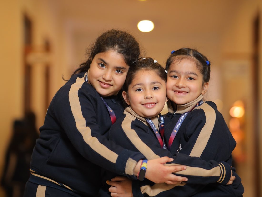 Three students hugging and smiling in the school hallway at Infinia World School