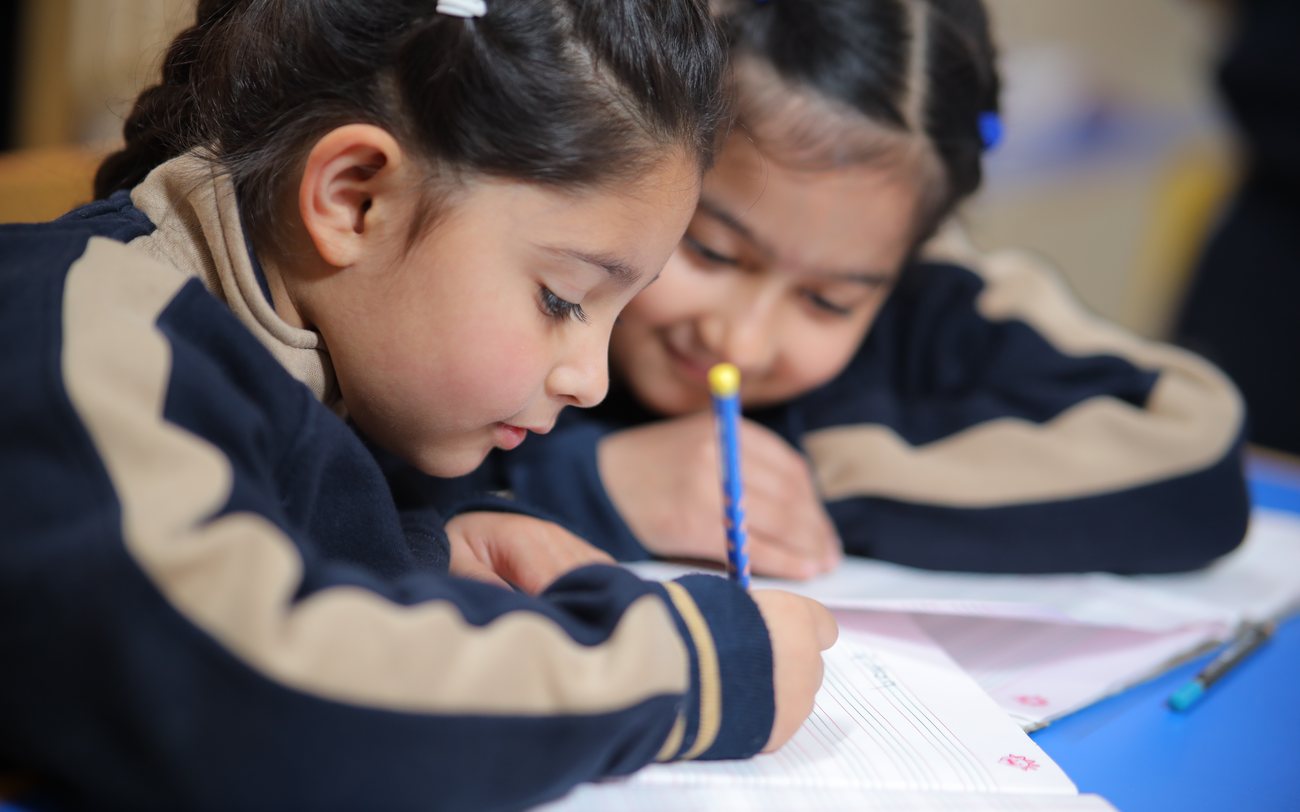 Two students focused on their writing, working side by side at Infinia World School